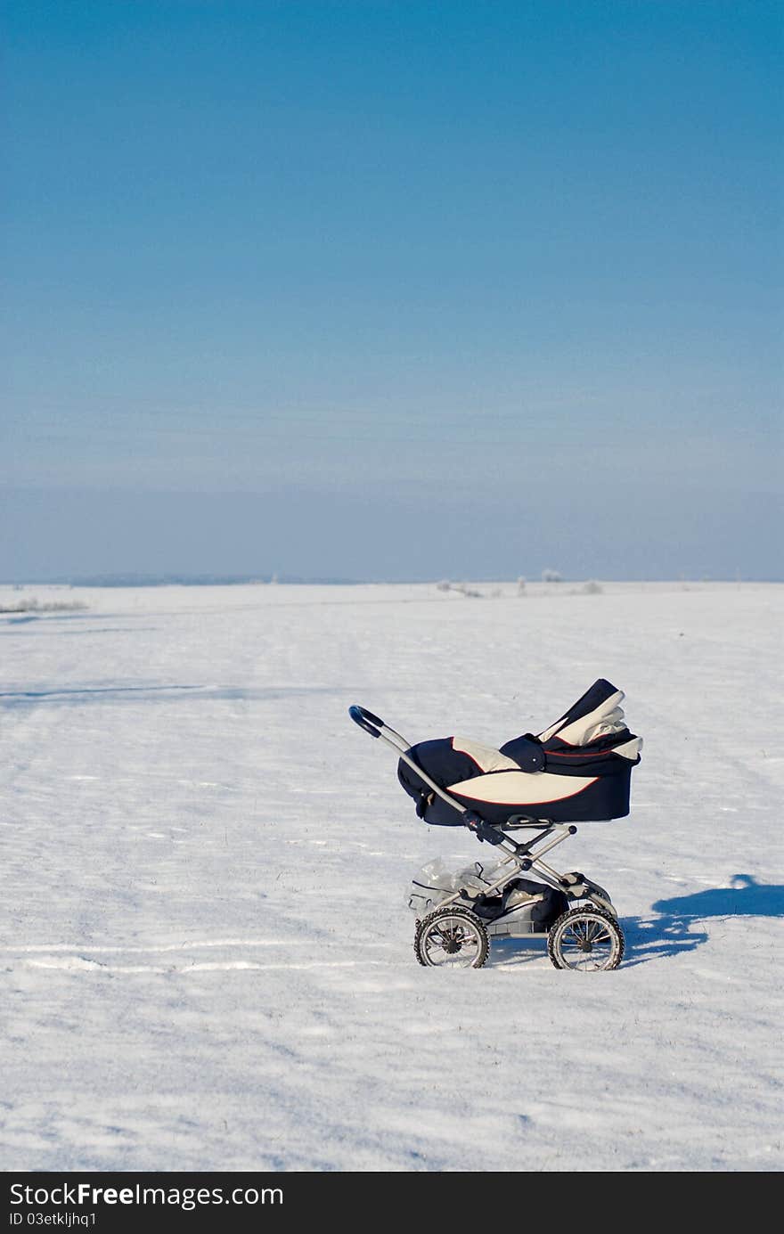 A baby buggy standing alone in the snowy fields under blue peacefull sky. A baby buggy standing alone in the snowy fields under blue peacefull sky.