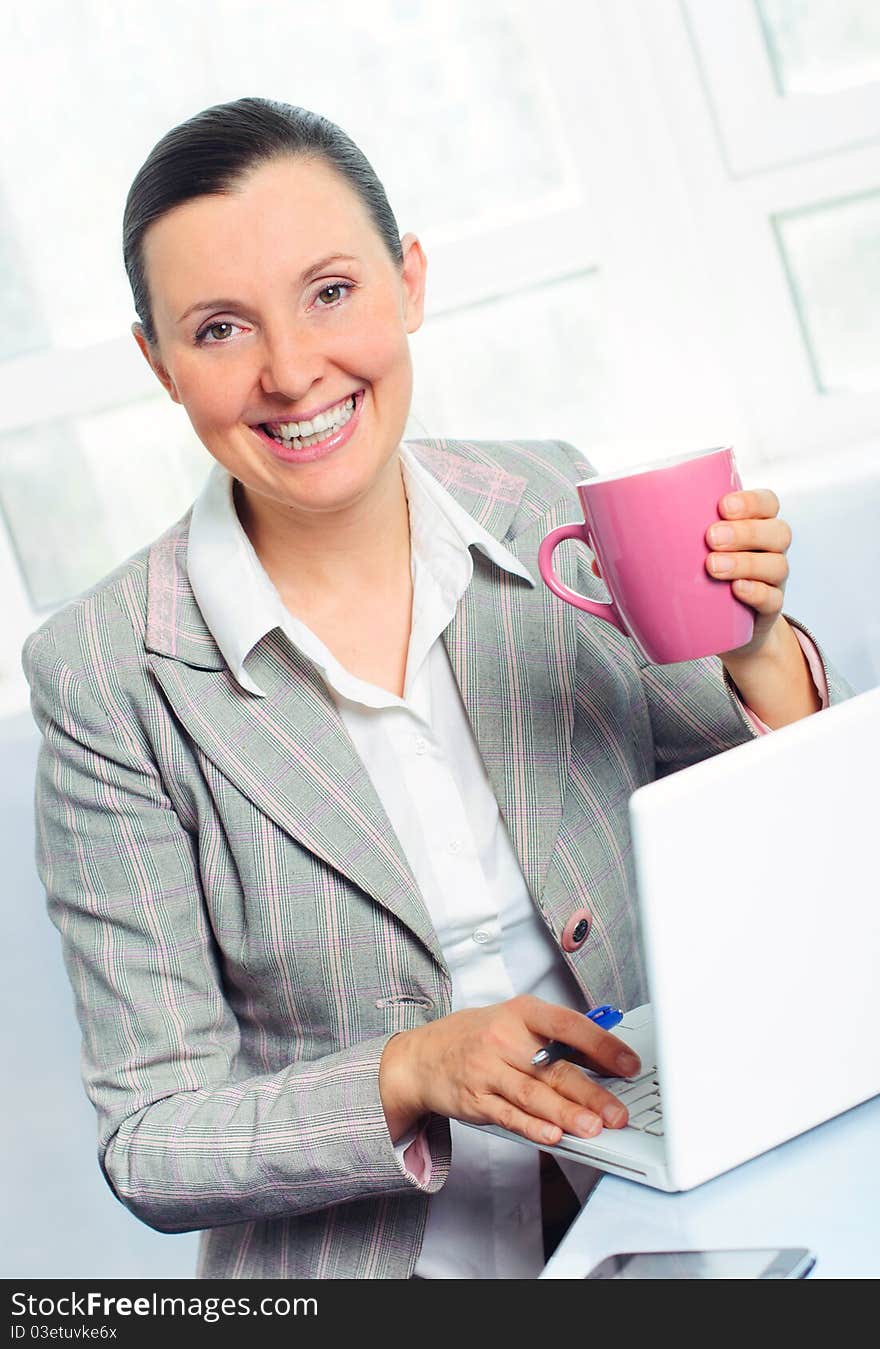 Attractive smiling young business woman with cup using laptop at work desk