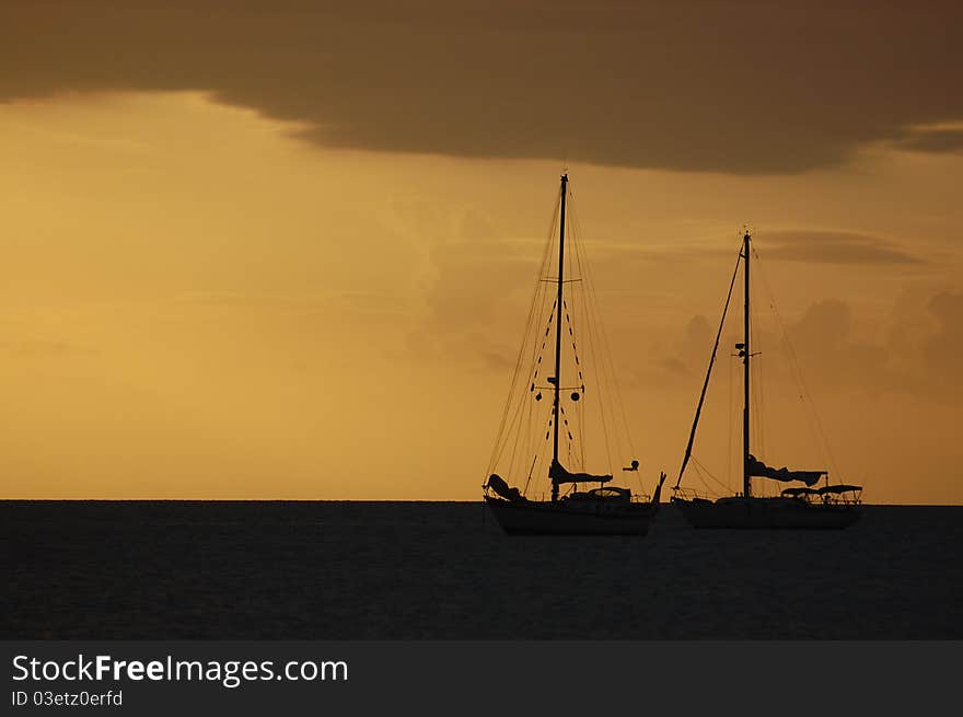 Two sailboats sit in calm waters at sunset. Two sailboats sit in calm waters at sunset.