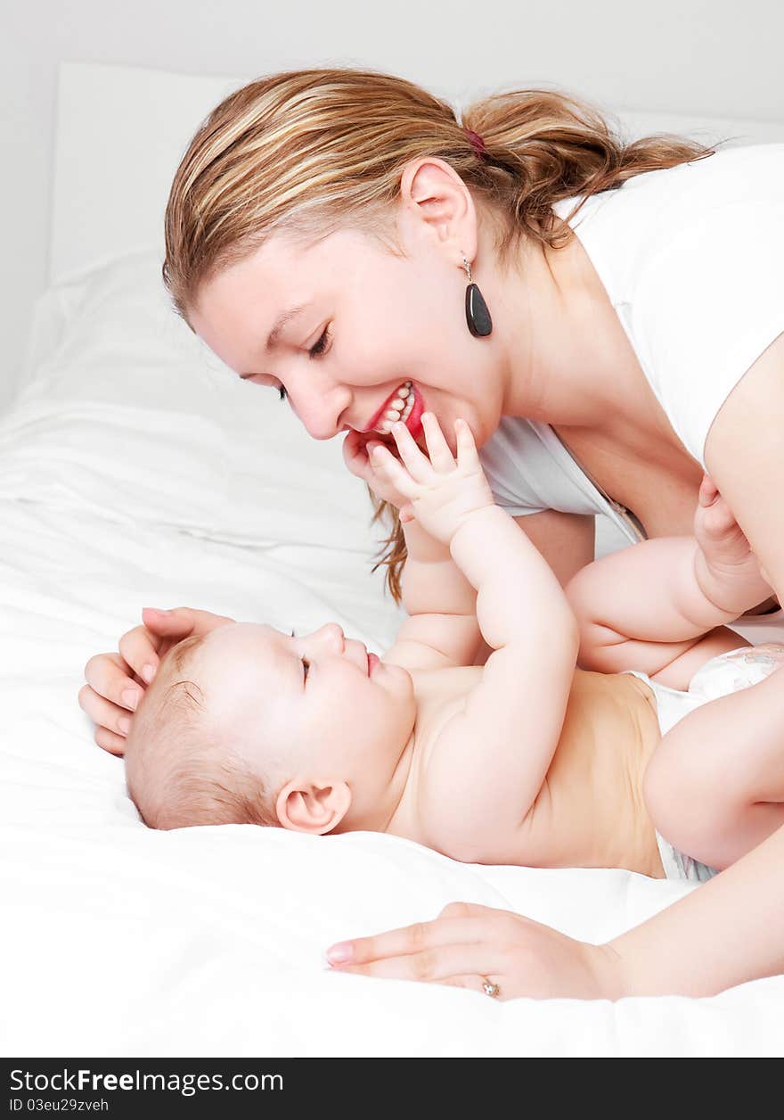 Young  mother and her six months old baby on the bed at home. Young  mother and her six months old baby on the bed at home