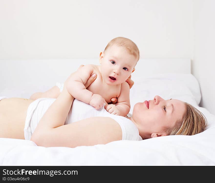 Young mother and her six months old baby on the bed at home. Young mother and her six months old baby on the bed at home