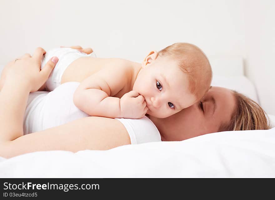 Young  mother and her six months old baby on the bed at home. Young  mother and her six months old baby on the bed at home