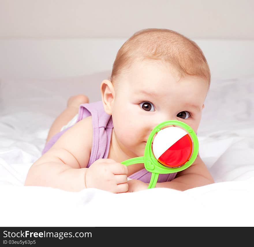 Cute six months old baby on the bed with a toy