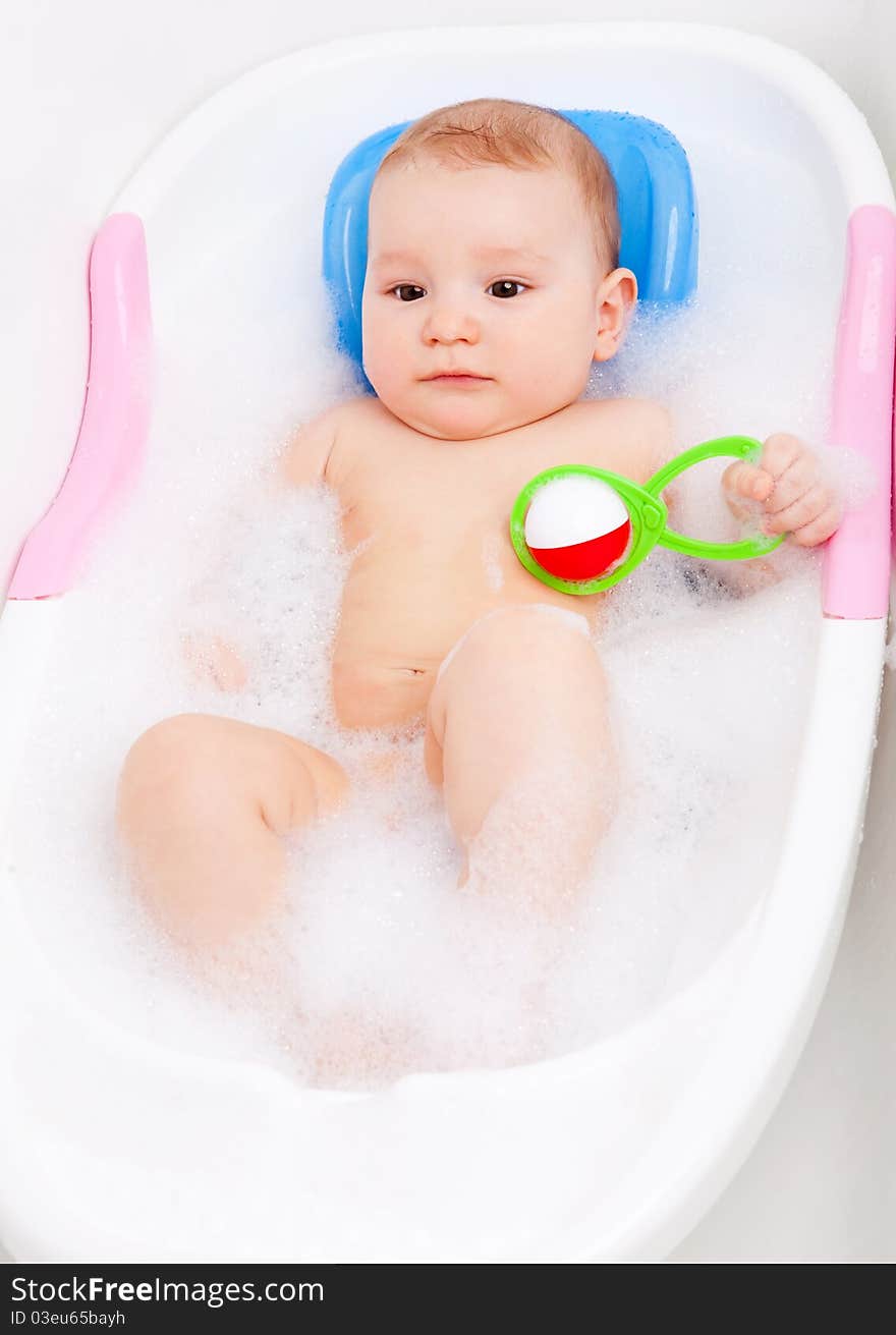 Cute six months old baby taking a bath with foam and playing with a toy