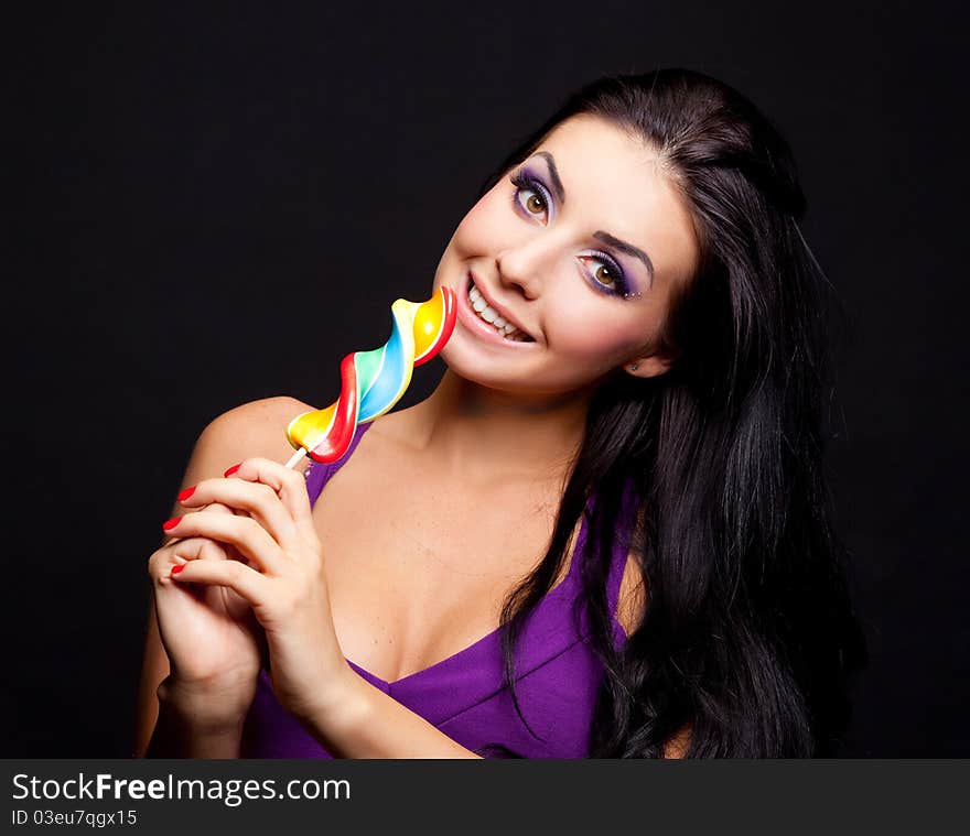 Pretty brunette girl with a lollipop, isolated against black background