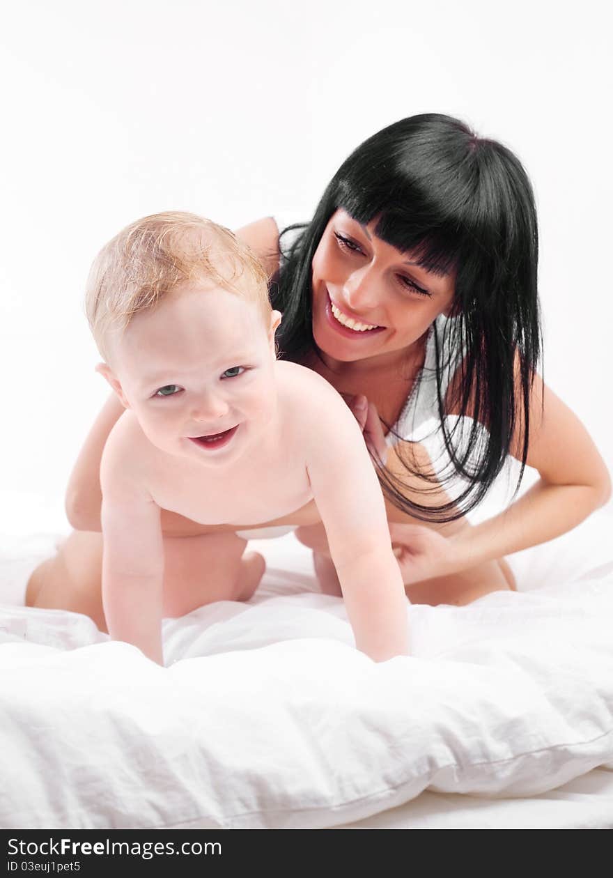 Happy young mother and her baby on the bed at home (focus on the baby). Happy young mother and her baby on the bed at home (focus on the baby)