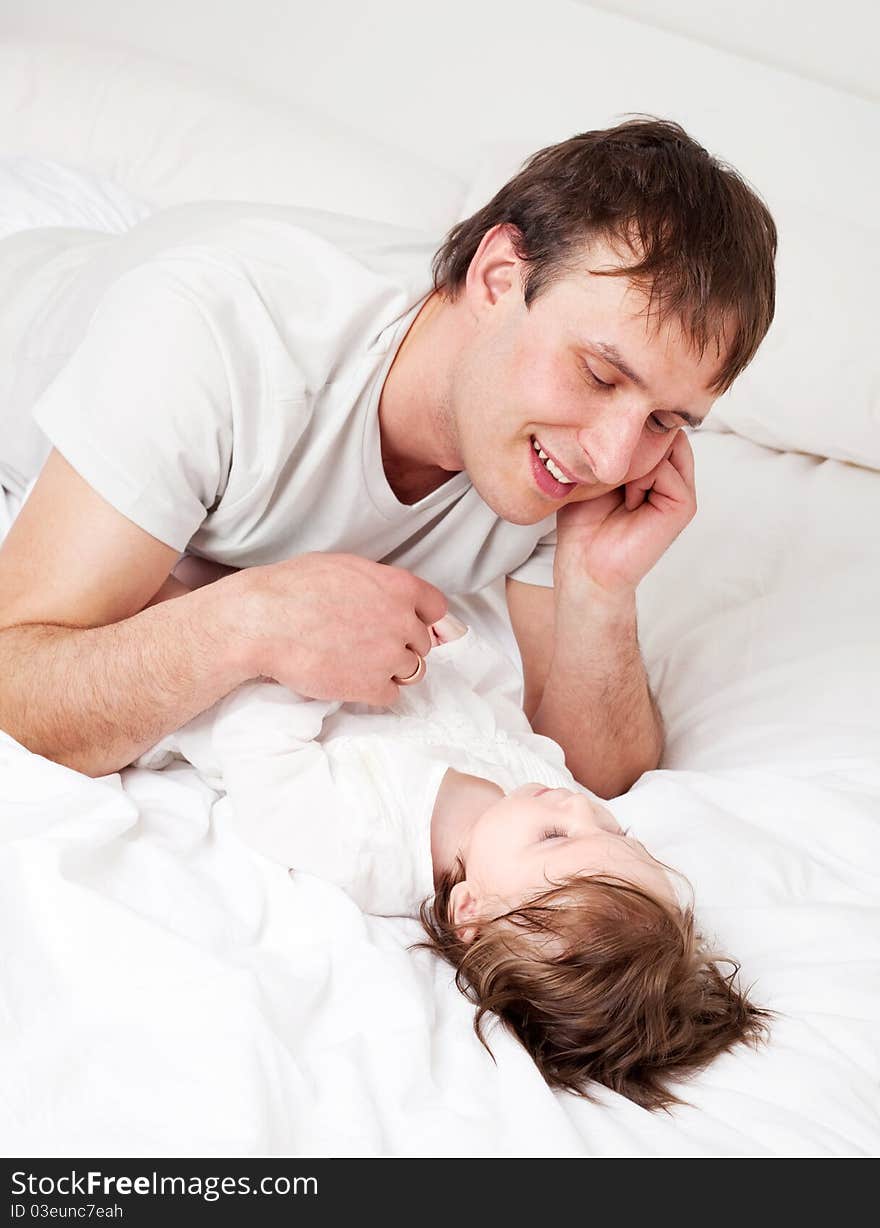 Young father with his six months old daughter on the bed at home (focus on the man). Young father with his six months old daughter on the bed at home (focus on the man)