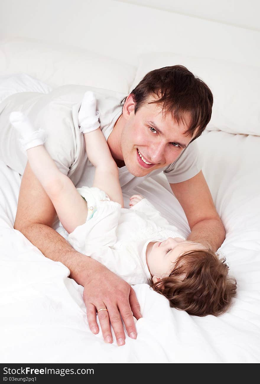 Young father with his six months old daughter on the bed at home (focus on the man). Young father with his six months old daughter on the bed at home (focus on the man)