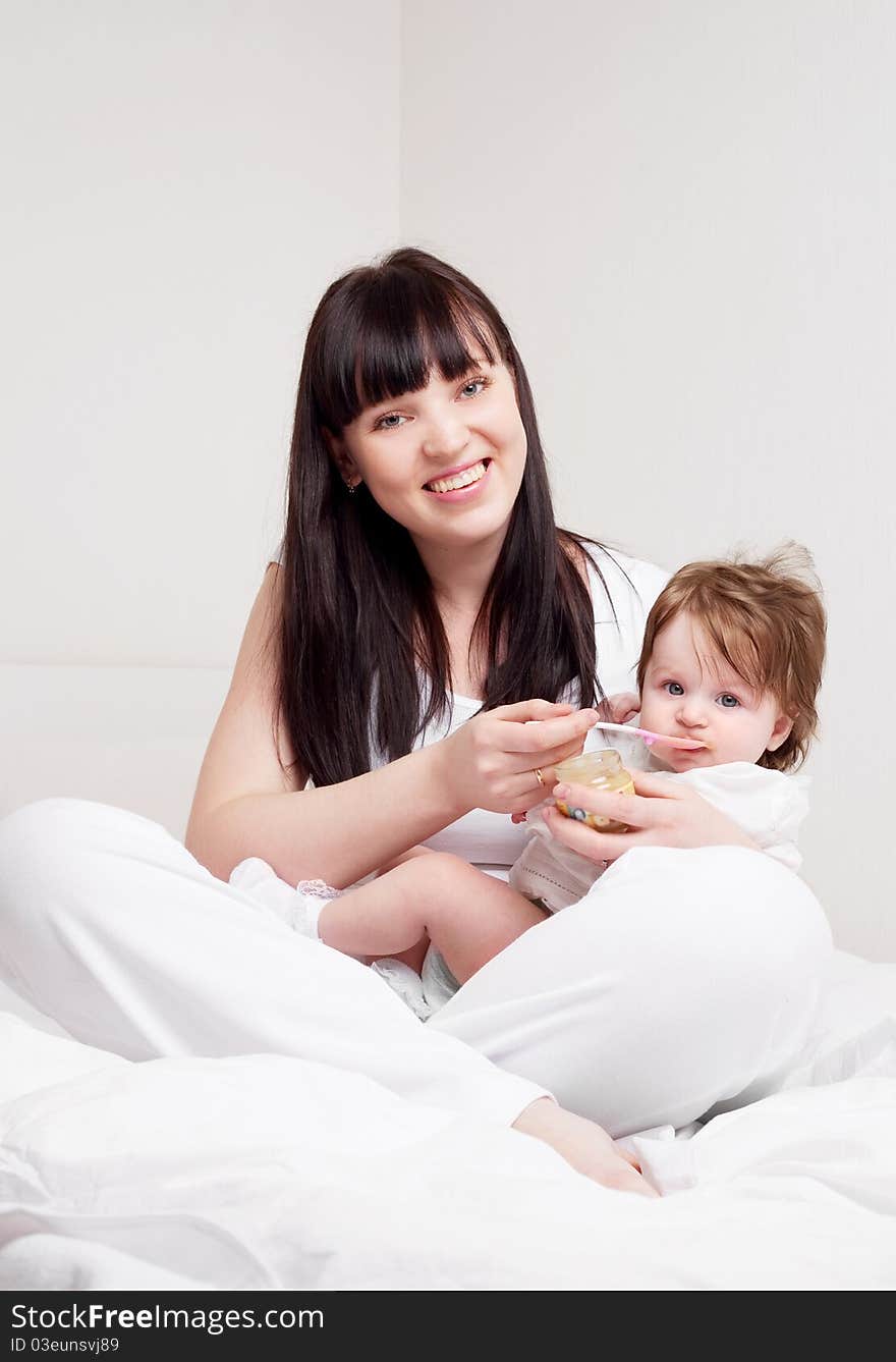 Happy young mother feeding her baby with yogurt (focus on the mother). Happy young mother feeding her baby with yogurt (focus on the mother)