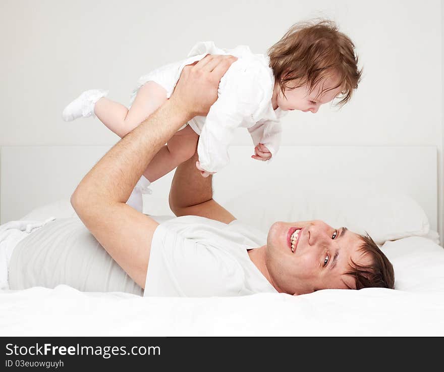 Young father with his six months old daughter on the bed at home (focus on the man). Young father with his six months old daughter on the bed at home (focus on the man)