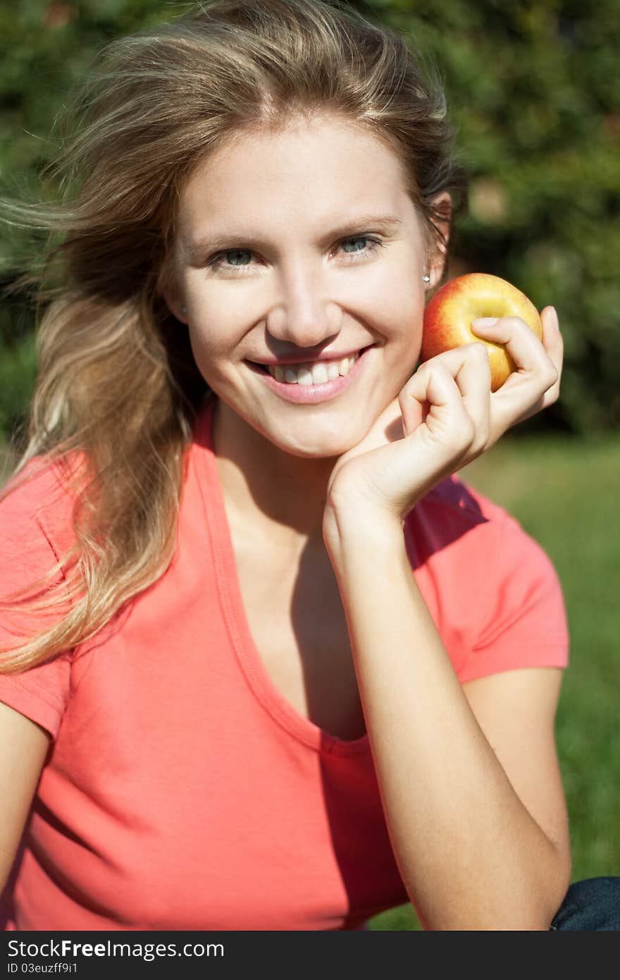 Beautiful young girl smiles happily with apple and beautiful white healthy teeth on the green grass on a sunny day