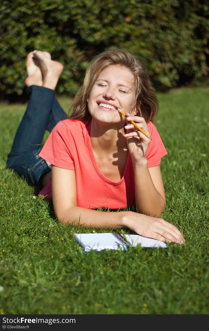 Young girl lying on the grass in summer and smiling, squinting in the sun. wrote in a notebook with a pencil. Young girl lying on the grass in summer and smiling, squinting in the sun. wrote in a notebook with a pencil.