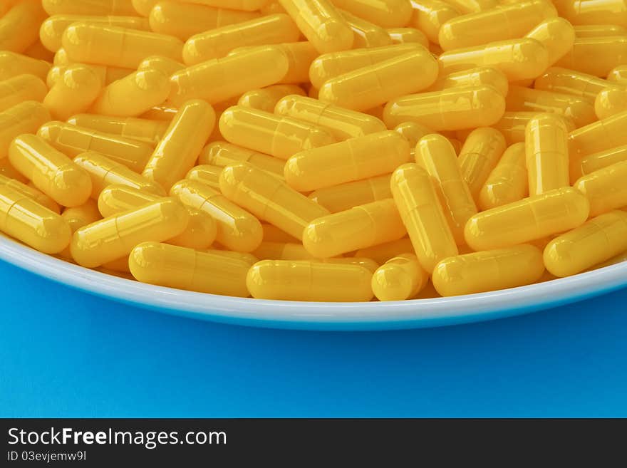 Yellow capsule pills on a white plate on blue black ground. Yellow capsule pills on a white plate on blue black ground