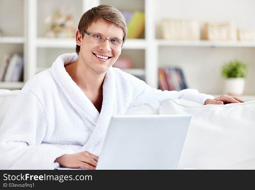 A man in a robe with a laptop at home. A man in a robe with a laptop at home