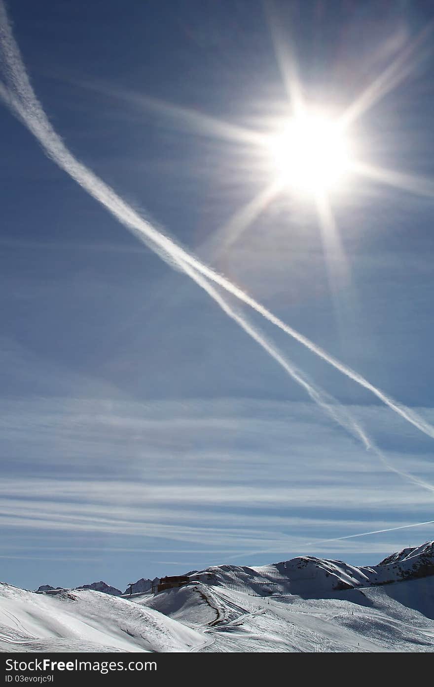 Bright Shining Sun with the trace of the plain on the blue sky under mountains with pistes and trails.