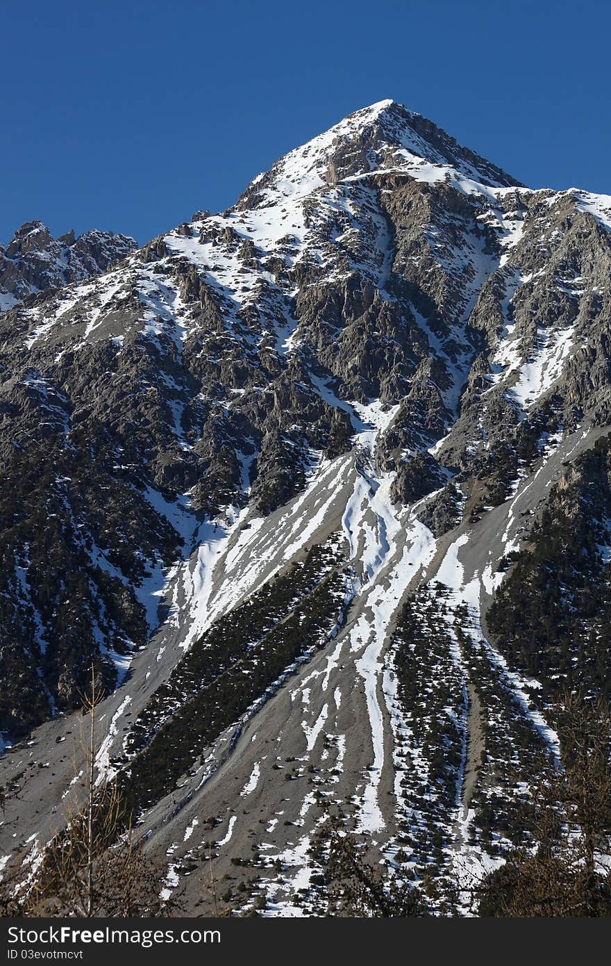 Big mountain peak on the blue sky with the risk of avalanches