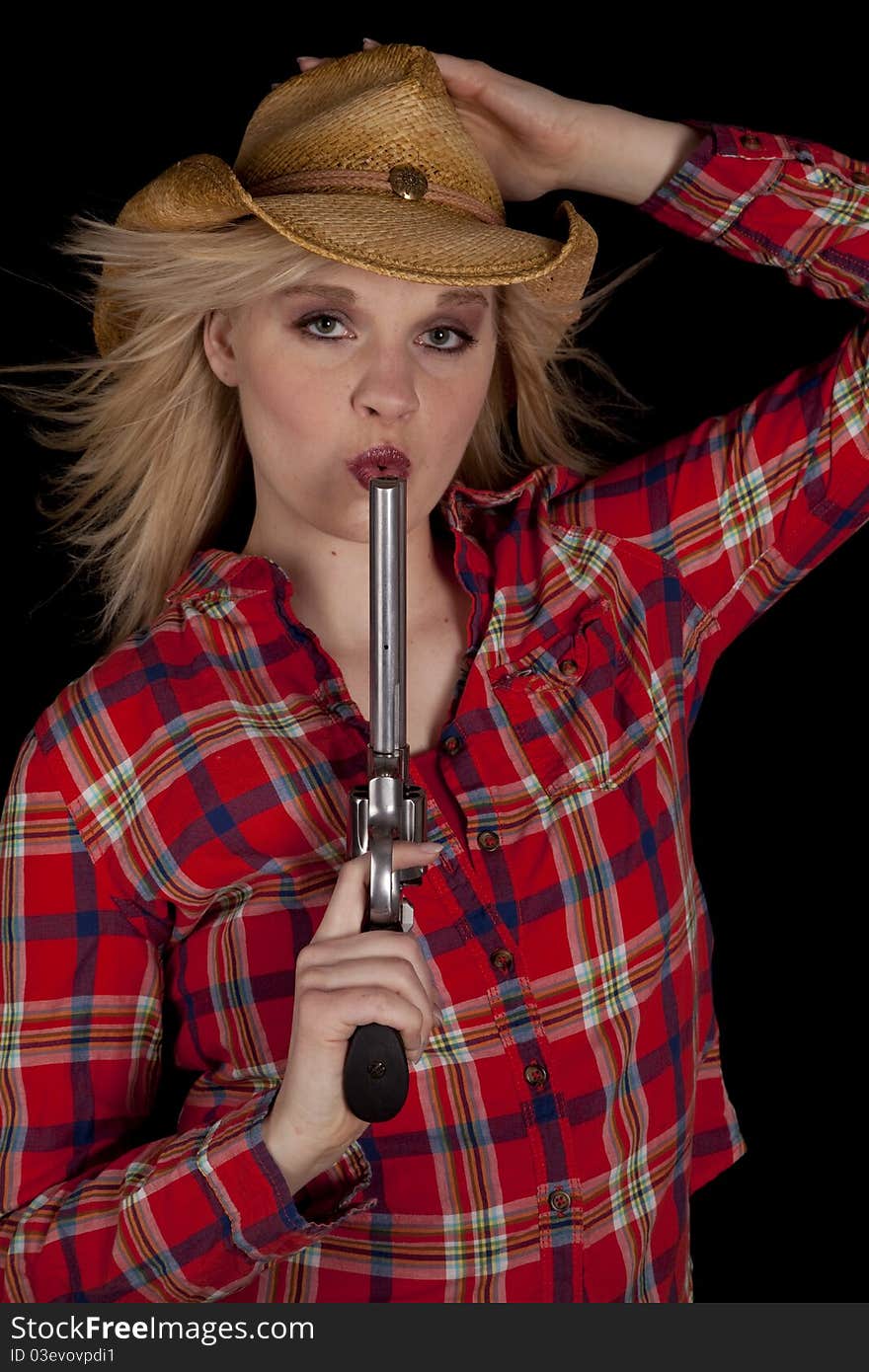 A cowgirl on a black background holding on to her hat while blowing on a pistols barrel. A cowgirl on a black background holding on to her hat while blowing on a pistols barrel.