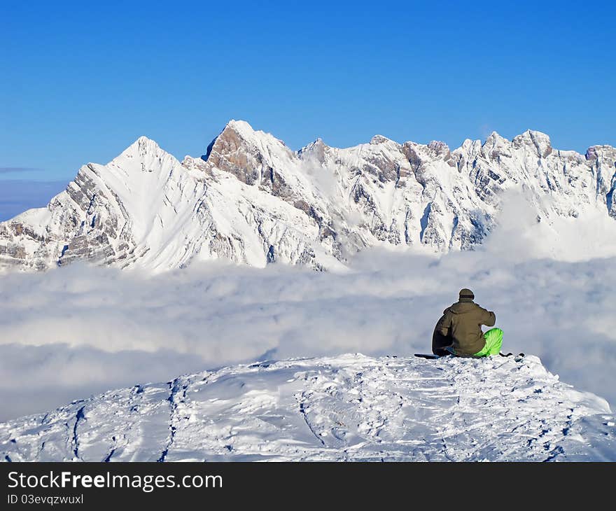 Two young snowboarders sitting on the peak over clouds. Two young snowboarders sitting on the peak over clouds