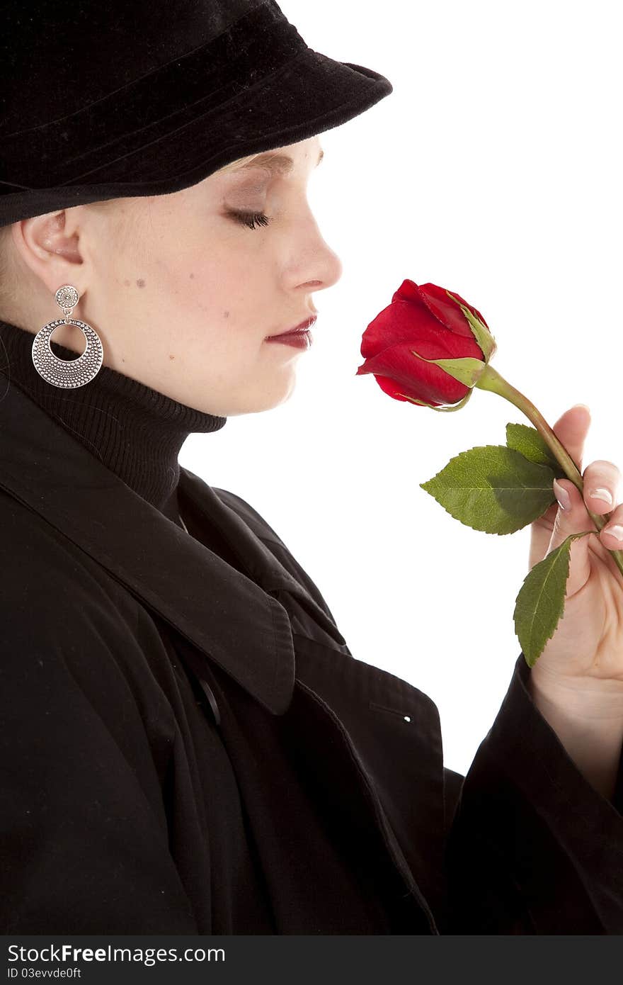 A side view of a girl in a black coat and hat smelling a red rose. A side view of a girl in a black coat and hat smelling a red rose.