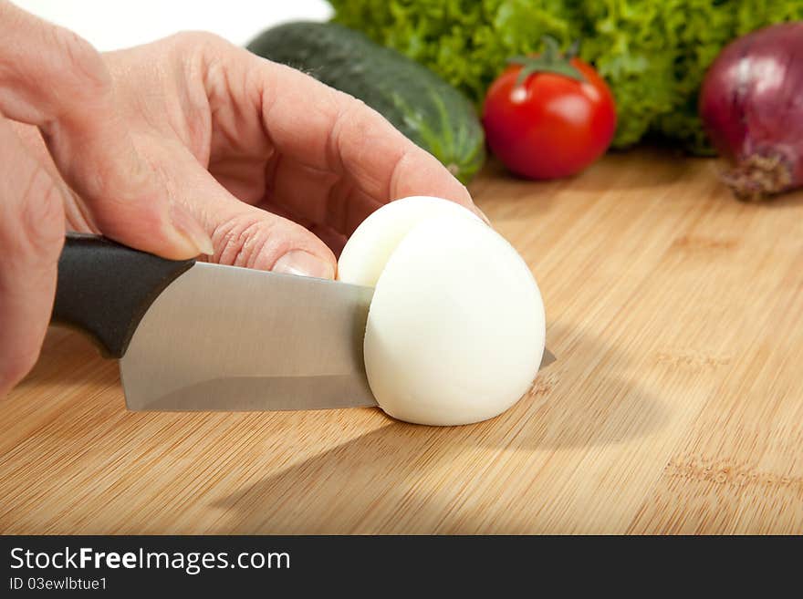 A woman is cutting an egg in preparation for a salad. A woman is cutting an egg in preparation for a salad.