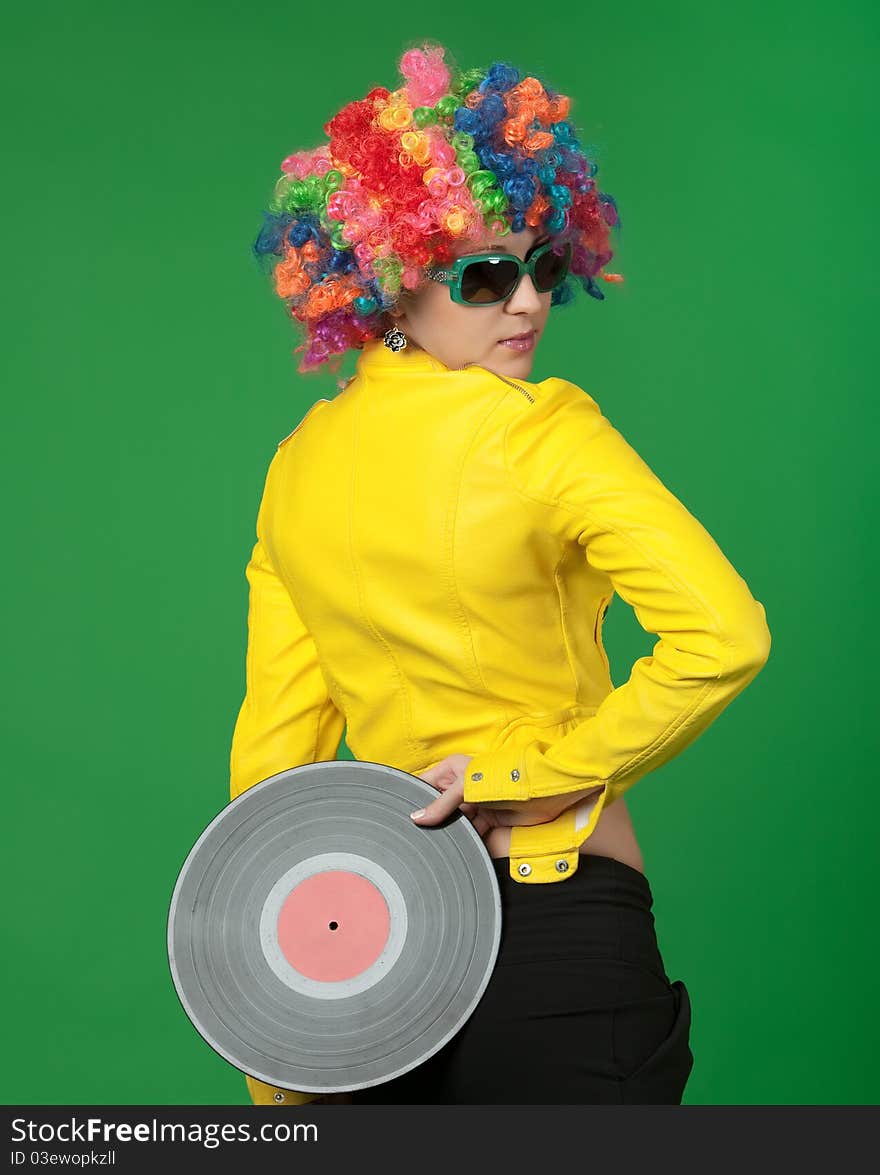 The girl in a color wig with a disk on green background. The girl in a color wig with a disk on green background