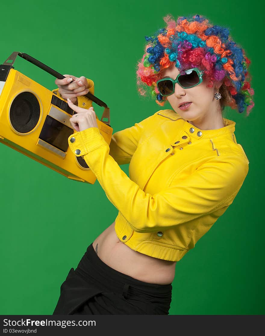 The girl in a color wig with the old tape recorder on green background. The girl in a color wig with the old tape recorder on green background