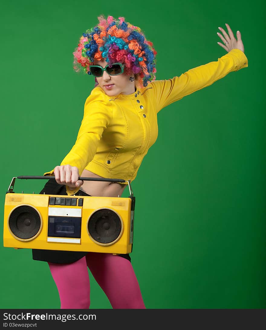 The girl in a color wig with the old tape recorder on green background. The girl in a color wig with the old tape recorder on green background