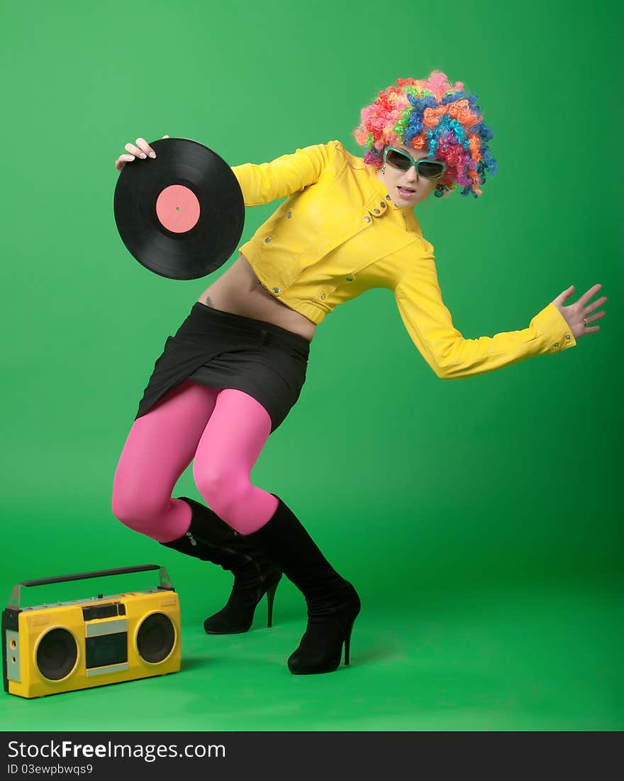 The girl in a color wig with a disk the old tape recorder on green background. The girl in a color wig with a disk the old tape recorder on green background