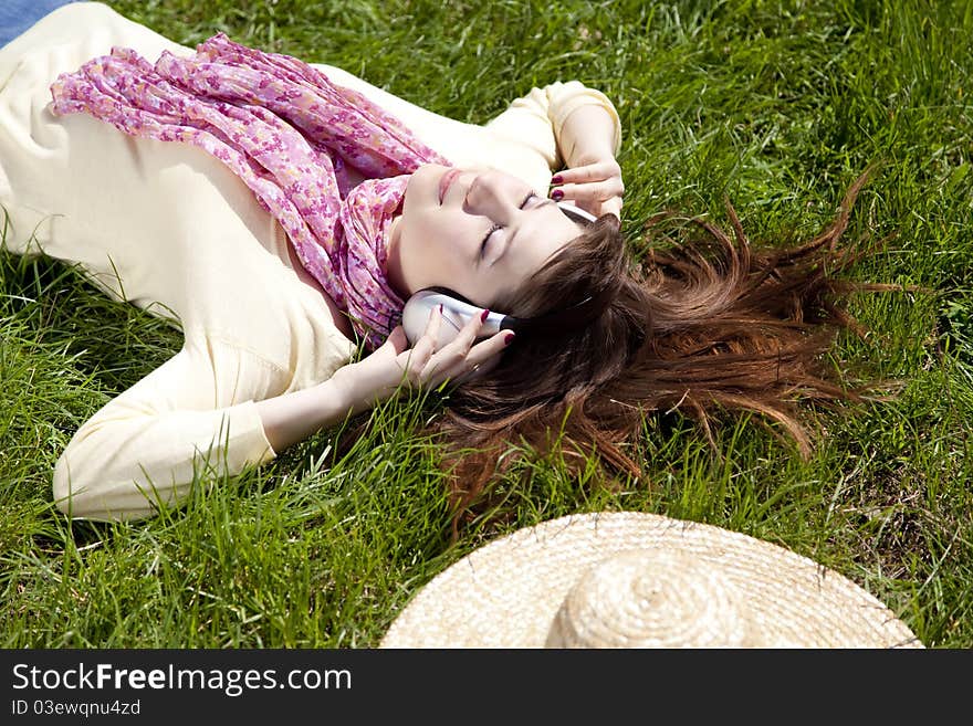 Brunette girl with headphone lies in the park.