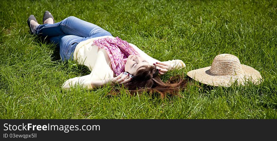 Brunette girl with headphone lies in the park.