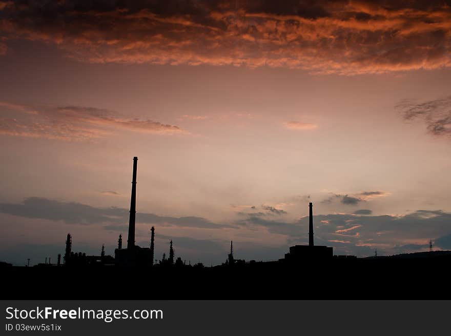 Silouethe of an oil factory with two chimneys, under a dramatic orange sky, photographed at dusk. Silouethe of an oil factory with two chimneys, under a dramatic orange sky, photographed at dusk.