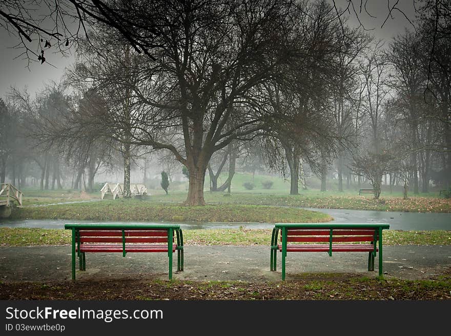 Autumn morning scene of two lonely red benches in an empty misty park. Autumn morning scene of two lonely red benches in an empty misty park.