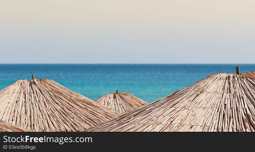 An abstract composition consisting of three straw sun umbrellas. The sea is blured in the background. Shallow depth of field.