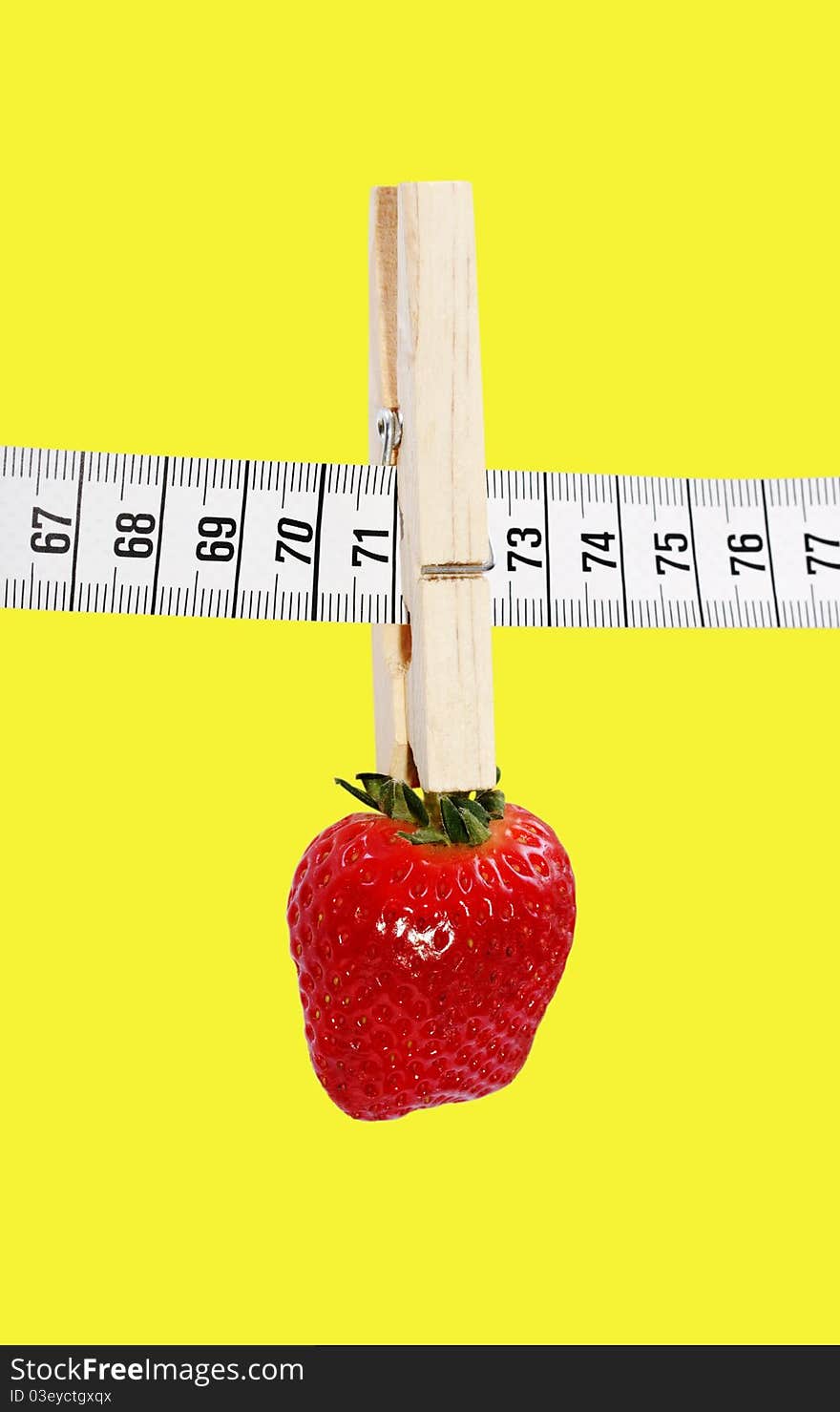 One strawberry hanging on the measuring tape with clothespin isolated on a yellow surface. One strawberry hanging on the measuring tape with clothespin isolated on a yellow surface.