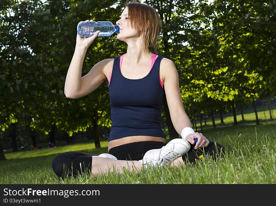 Young girl sitting on the grass drinking water