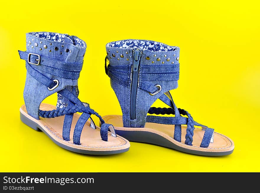 Children sandals sewn from denim stand against a yellow background. Children sandals sewn from denim stand against a yellow background