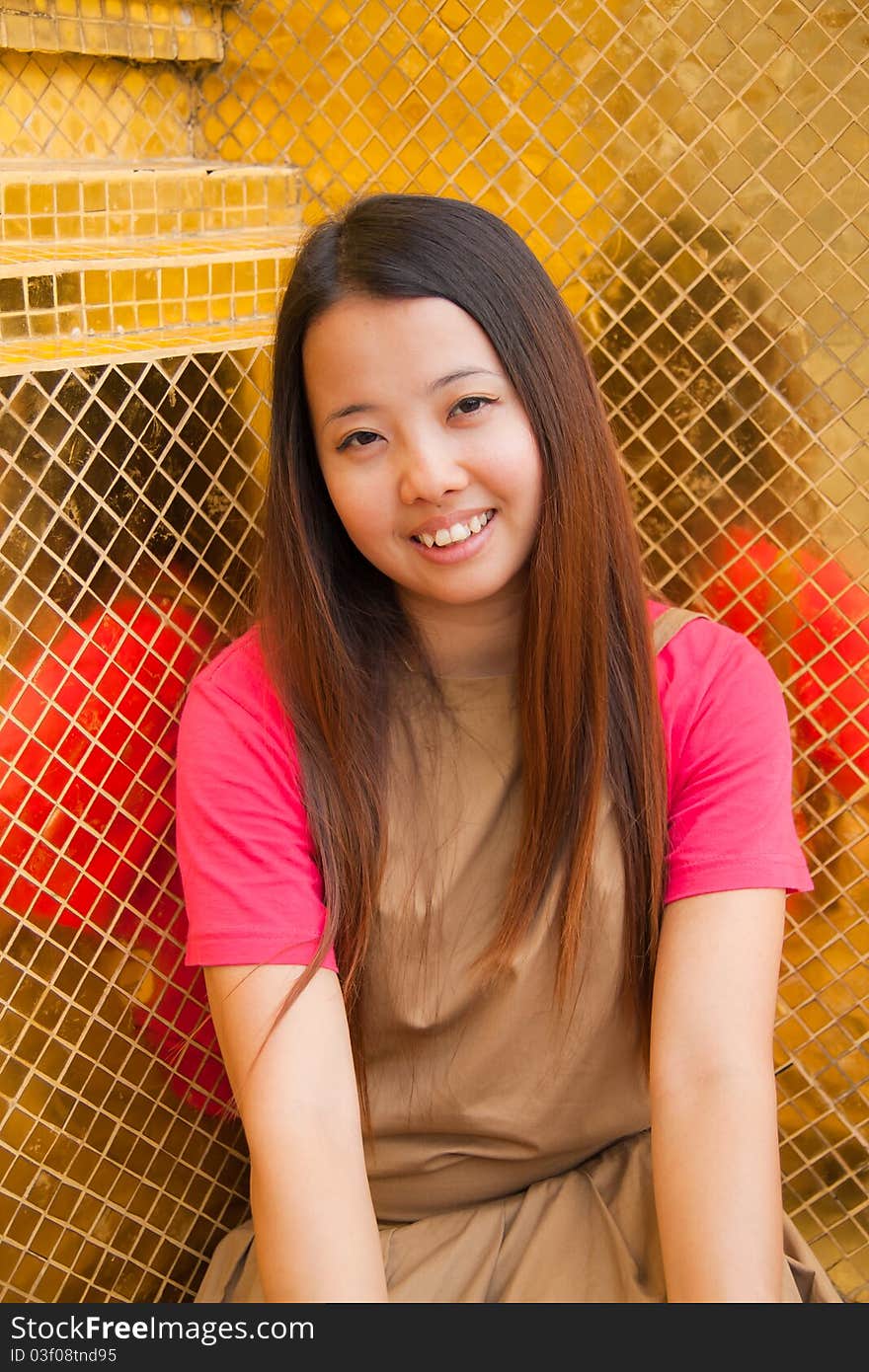 Young Thai women sitting and smiling with golden tile in background with space on top left