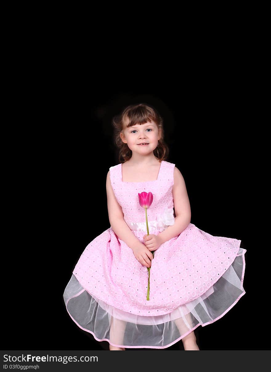 Sweet little girl sitting down with single pink tulip in her hand isolated on black. Sweet little girl sitting down with single pink tulip in her hand isolated on black