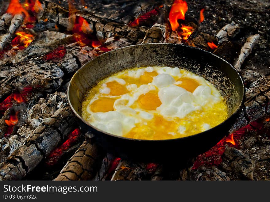 Hiking pan standing on the coals with a roasting in her scrambled eggs. Hiking pan standing on the coals with a roasting in her scrambled eggs.