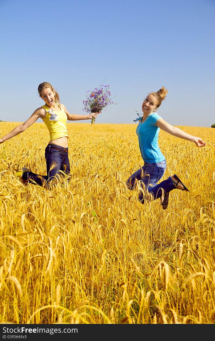 Two beautiful girls jumps in golden field