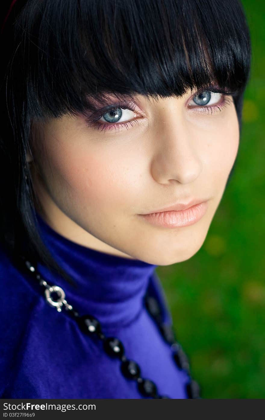 Portrait of attractive young woman with black hair; green nature background