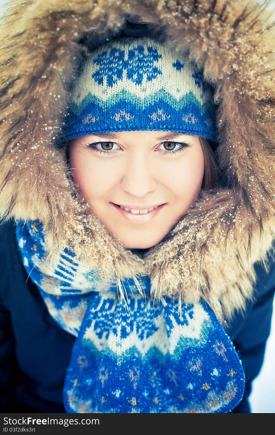 Attractive young woman in wintry coat with large fur head, snowy in background.