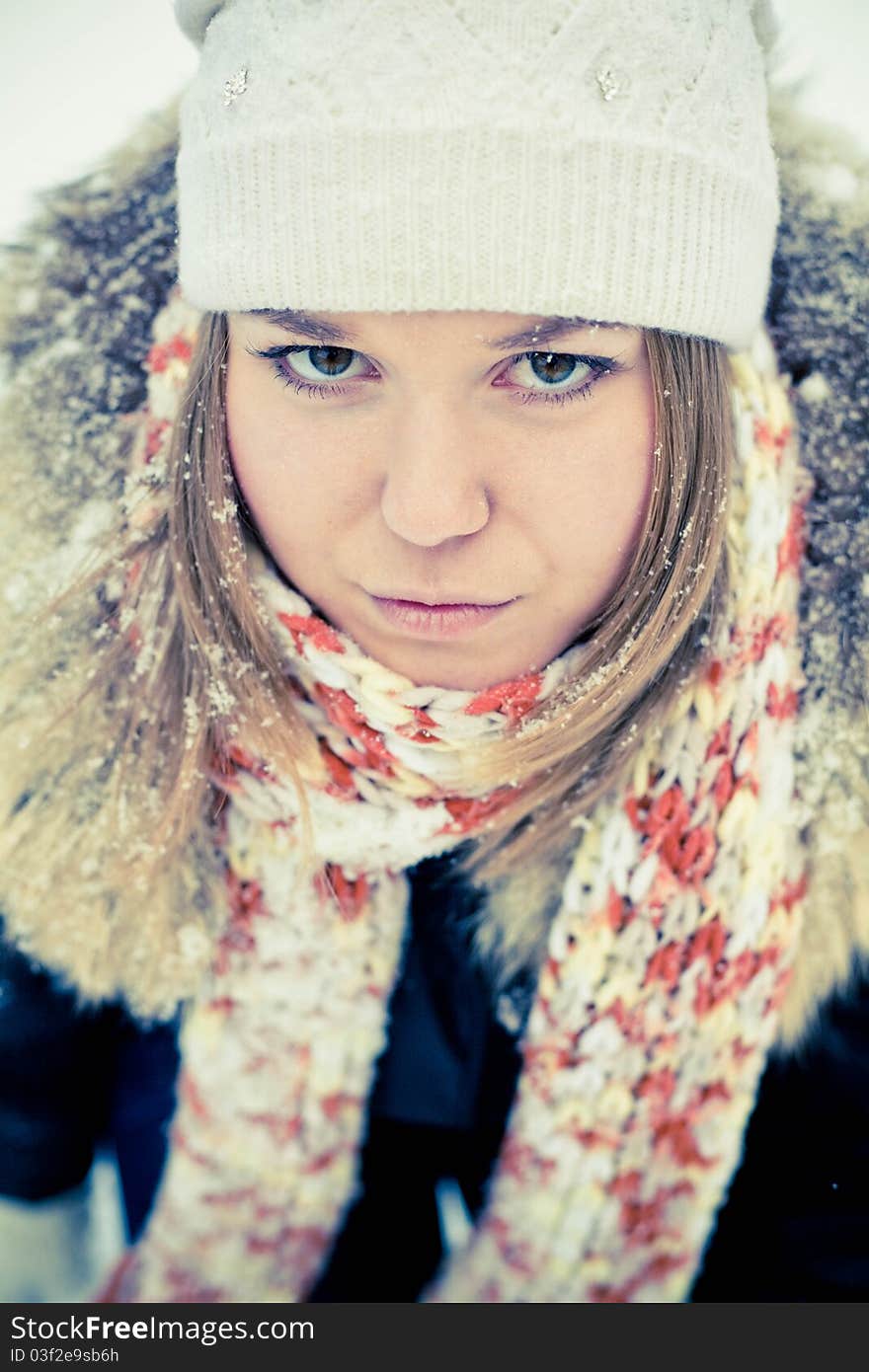 Attractive young woman in wintry coat with large fur head, snowy in background.