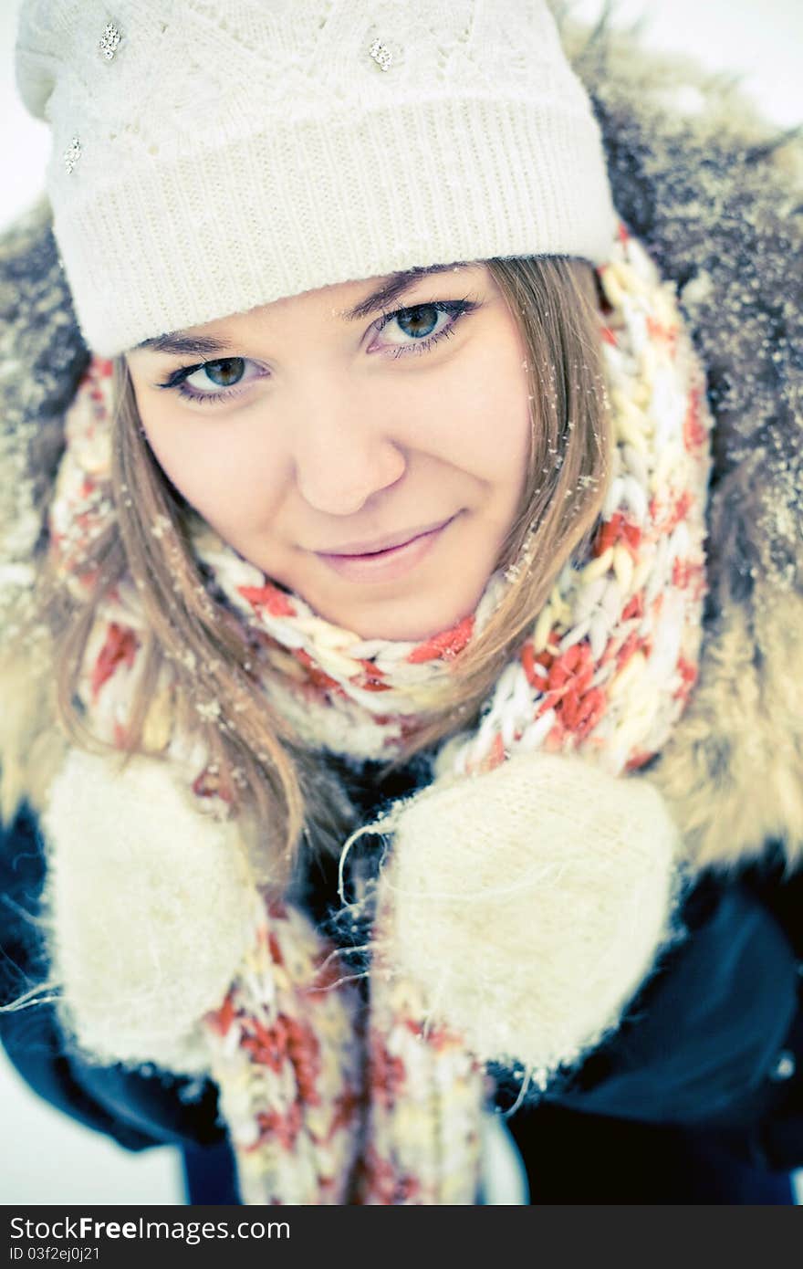 Attractive young woman in wintry coat with large fur head, snowy in background.