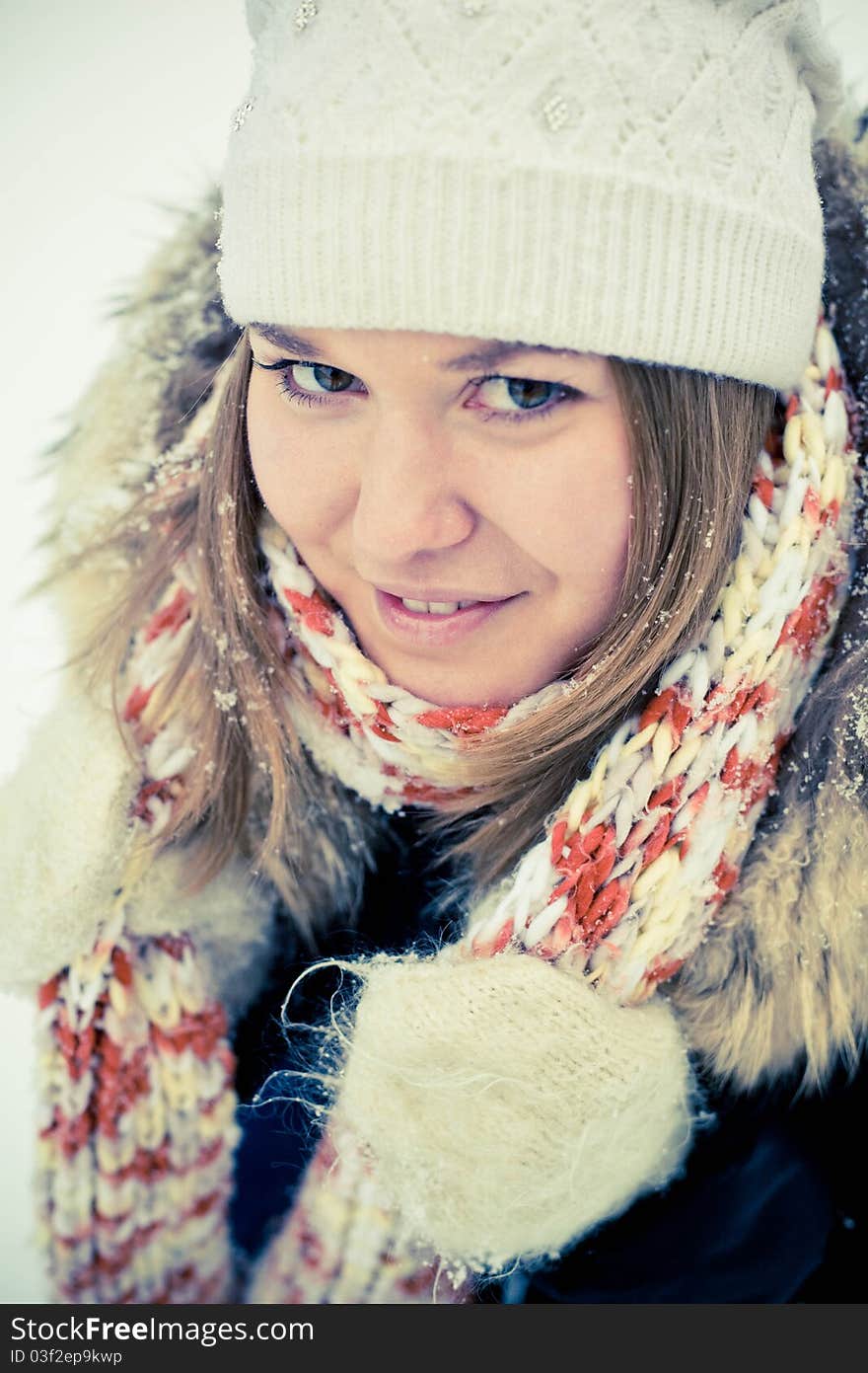 Attractive young woman in wintry coat with large fur head, snowy in background.