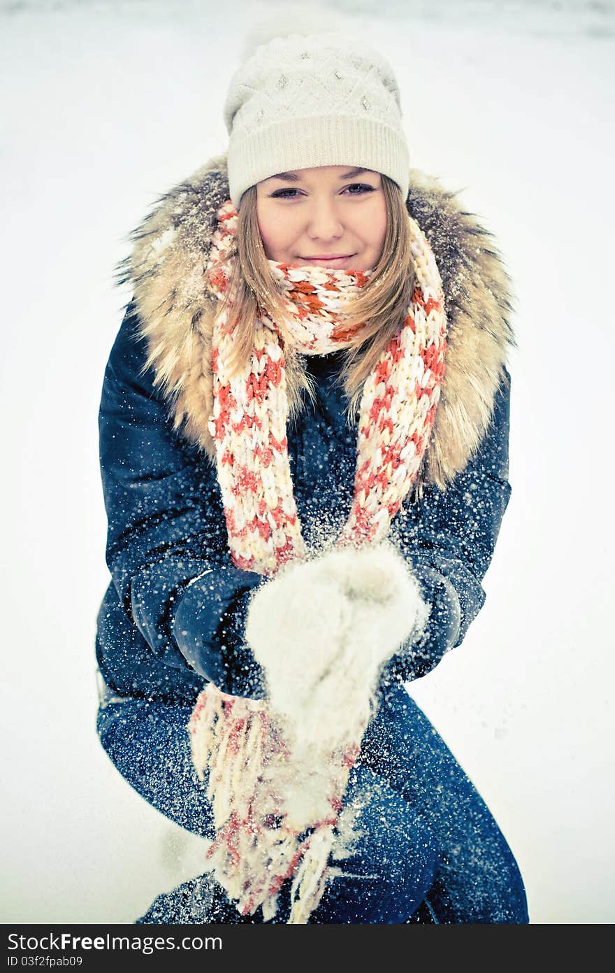 Attractive young woman in wintry coat with large fur head, snowy in background.