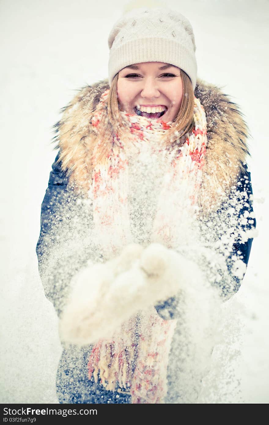 Attractive young woman in wintry coat with large fur head, snowy in background.