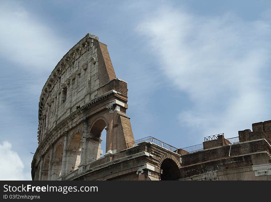 Daytime image of the Roman Coliseum with bright sun and partly cloudy skys.