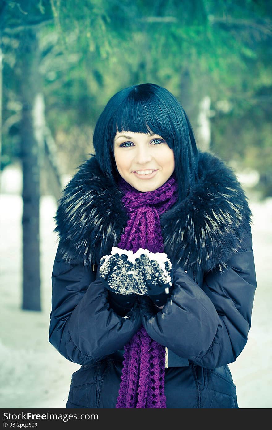 Attractive young woman in wintry coat with large fur head, snowy in background.