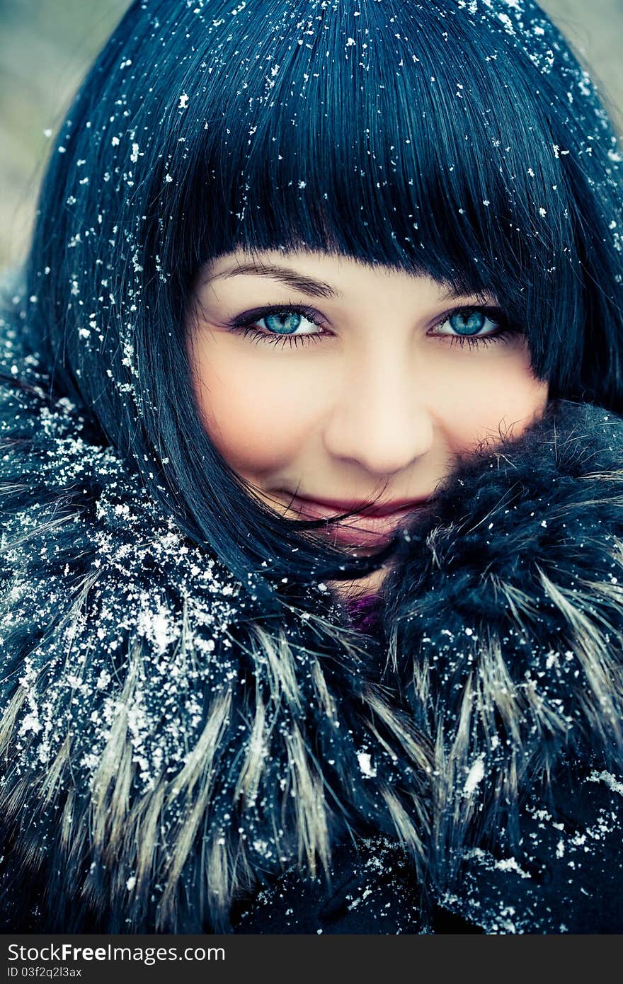 Attractive young woman in wintry coat with large fur head, snowy in background.